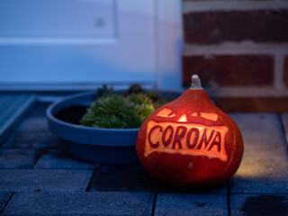 A carved illuminated pumpkin with corona lettering laying in front of a house entrance
