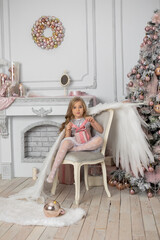 Little cute girl with blond hair with angel wings in the studio next to the Christmas tree and with Christmas balls