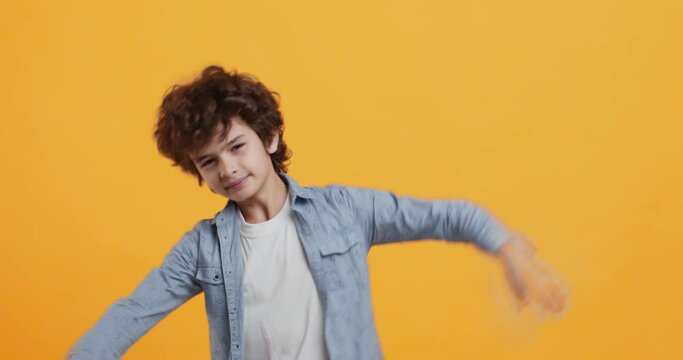 Trendy curly boy dancing, making dab gesture, having fun on orange background