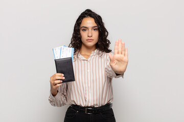 young hispanic woman looking serious, stern, displeased and angry showing open palm making stop gesture