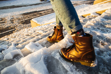 Winter is coming. Female boots on rough slipper ice surface. A woman in brown leather shoes...