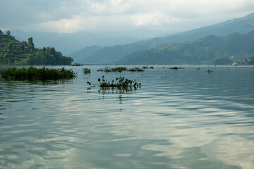 Waves on the surface of the lake water. Buildings on the shore. In the distance, the mountains are lost in the fog. Massive clouds above them