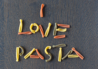 I love pasta written with tricolor caserecce Italian pasta, dressed with basil on a wooden table, top view