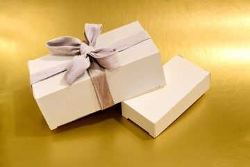 White gift box with gray ribbon and bow on a gold background close-up. Concept of holiday gifts for christmas, new year, birthday.