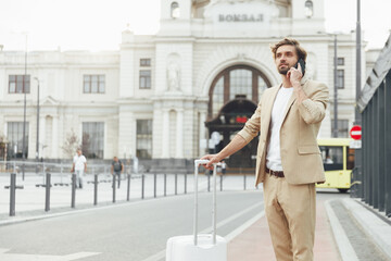 Man standing with suitcase near station an talking on mobile