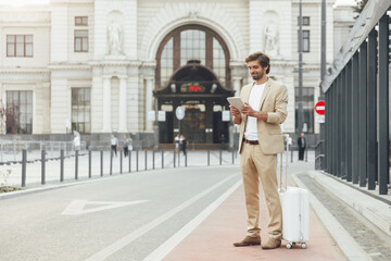 Bearded man in suit holding digital tablet near station