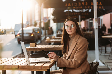 Close-up of young professional business woman using her laptop outside while working at modern business center, modern buildings in the background.