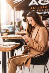 Happy pretty brunette girl using mobile phone near office, beautiful woman browsing phone and doing online shopping in a mobile app while smiling walking near shopping mall.