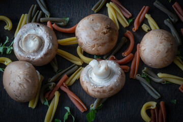 cave mushrooms or chestnut mushrooms with Tricolore Caserecce Italian pasta with 3 colors and dwarf basil leaves as a composition on wooden table 
