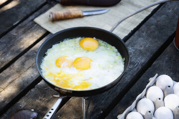 Cooking breakfast eggs on camping stove. Tourism recreation outside.
