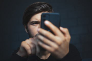 Close-up portrait of young man using smartphone on dark background.