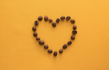 High resolution coffee beans arranged in heart shape on yellow background.Top view with copy space for text