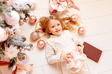 Cute little blonde girl in retro dress lies near the Christmas tree, view from above, space for text