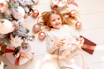 Cute little blonde girl in retro dress lies near the Christmas tree, view from above, space for text