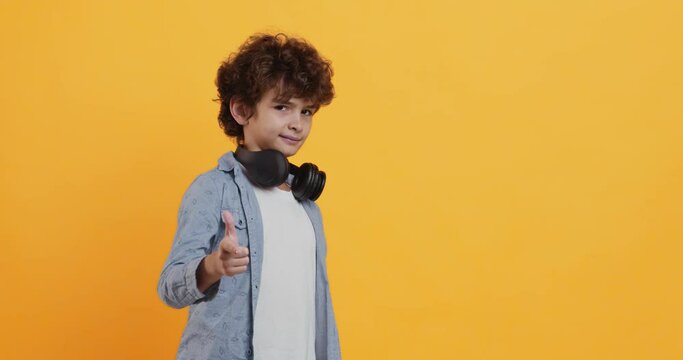 Cool curly boy with headphones on neck indicating happily at camera, flirt concept