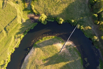Aerial view of a simple suspension bridge over a small river. Summer landscape