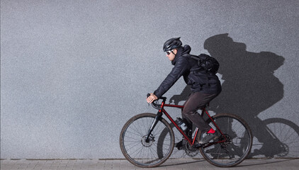 Young man in casual clothes rides a bicycle against the background of a gray concrete wall. Side view. Urban style. Bicycle commuting concept.