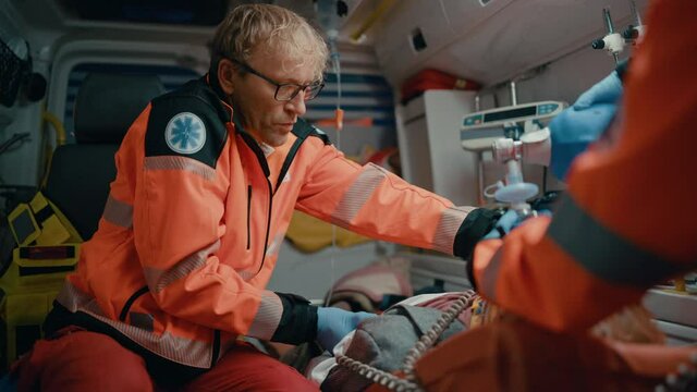 EMS Paramedics Team Provide Medical Help to Injured Patient on the Way to Hospital. Emergency Care Assistants Using a Defibrillator and Ventilation Mask to Bring the Man Back to Life in an Ambulance.