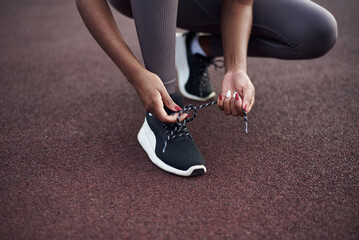 The girl ties the laces on black sneakers on the playground. Sports and healthy lifestyle concept