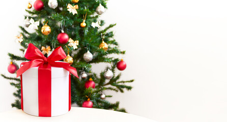 Fototapeta na wymiar Christmas gift box near Christmas tree. Big round white gift box with red ribbon. Copy space for text.