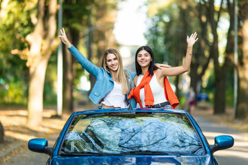 Two attractive young women in a convertible car have fun