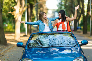 Young two women raising hands in convertible car