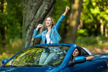 Young woman enjoy summer with raised hands standing in convertible car