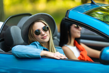 Two young happy women driving a cabriolet car. Summer vacations concept