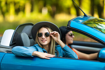 Two young happy women driving a cabriolet car. Summer vacations concept