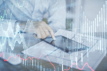 Double exposure of man's hands holding and using a digital device and forex graph drawing. Financial market concept.