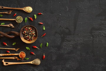 Different kind of spices on a black stone. Oriental spices in spoons, peppers, curry powder, herbs on black metallic tray in Asian style. Flat lay, top view.