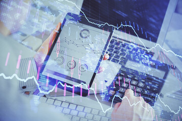 Double exposure of man's hands holding and using a digital device and forex graph drawing. Financial market concept.