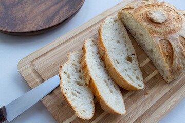 Composition in natural light. Homemade yeast-free bread (french bun) sliced on a wooden board, a knife and a dark wood plate nearby