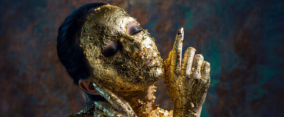 Girl with a mask on her face made of gold leaf. Gloomy studio portrait of a brunette on an abstract background.
