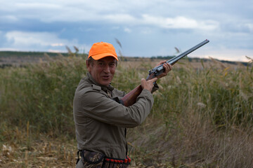 Fototapeta premium Duck hunter with shotgun walking through a meadow.