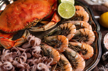 Close-up top view of round dish with assorted seafood. Cooked crab, baby octopuses and tiger shrimps served with sea salt, lime and seashells on rustic wooden background. Seafood concept. Delicious.