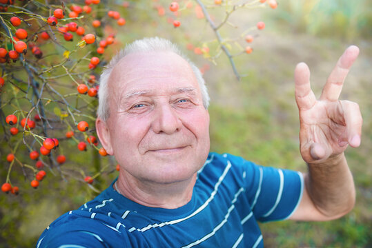 positive retired grandfather, makes selfie photo with a smartphone in the park. an elderly man walks in nature.