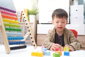 Cute little asian kindergarten 4 years old boy using the abacus with beads and wooden brick with numbers to learn how to count indoor at home, Use an Abacus to teach maths for little kids concept