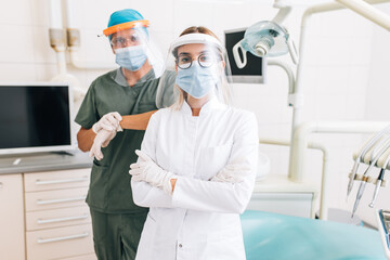 Portrait of dentist with young female assistant in full protective uniform at the dental office