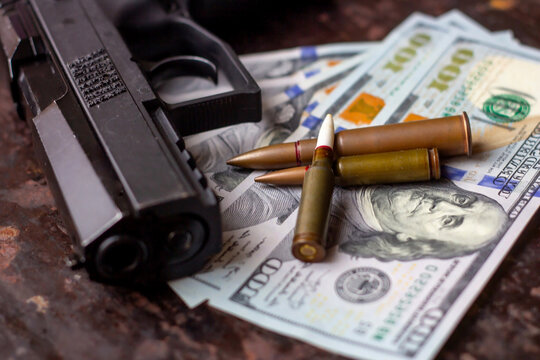 Black gun and bullets on American dollars background. Military industry, war, global arms trade, weapon sale, contract killing and crime concept.