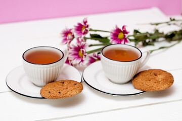 Two cups of tea and oatmeal cookies. pink chrysanthemums. Breakfast. Tea drinking. White wooden background.