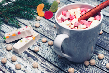 White mug of hot chocolate drink with marshmallow and cinnamon stick on wooden background, Christmas decorations. Nearby sweets and candies.