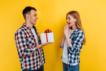 Happy young couple in love holding gift box on yellow background, Valentine's Day