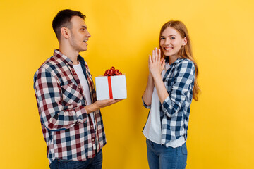 Happy young couple in love holding gift box on yellow background, Valentine's Day