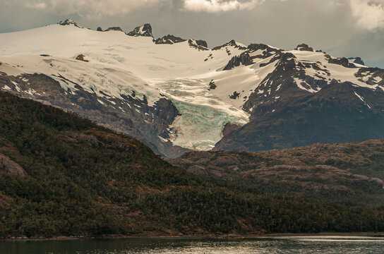 Sarmiento Channel, Chile - December 11, 2008: Flord and Amalia Glacier above belt of brown rocks and green foliage under white cloudscape, 