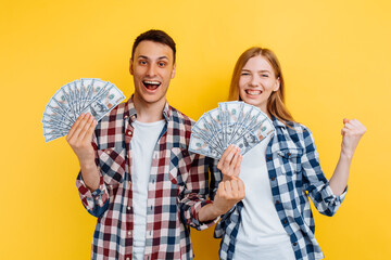 Excited couple, man and woman, holding dollar bills and celebrating isolated on yellow background