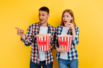 Happy man and woman eating popcorn while watching movie on yellow background