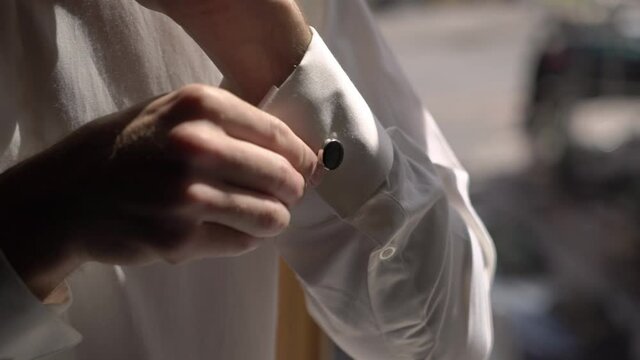 A young man puts cufflinks on a white shirt. The groom dresses in the morning