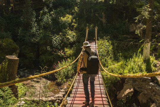 Fototapeta Boy scout, on a suspension bridge in the middle of the forest, carrying a backpack