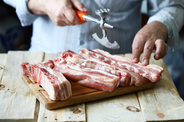 The chef cuts raw pork ribs on a wooden board. Selective focus. Cooking the ribs.